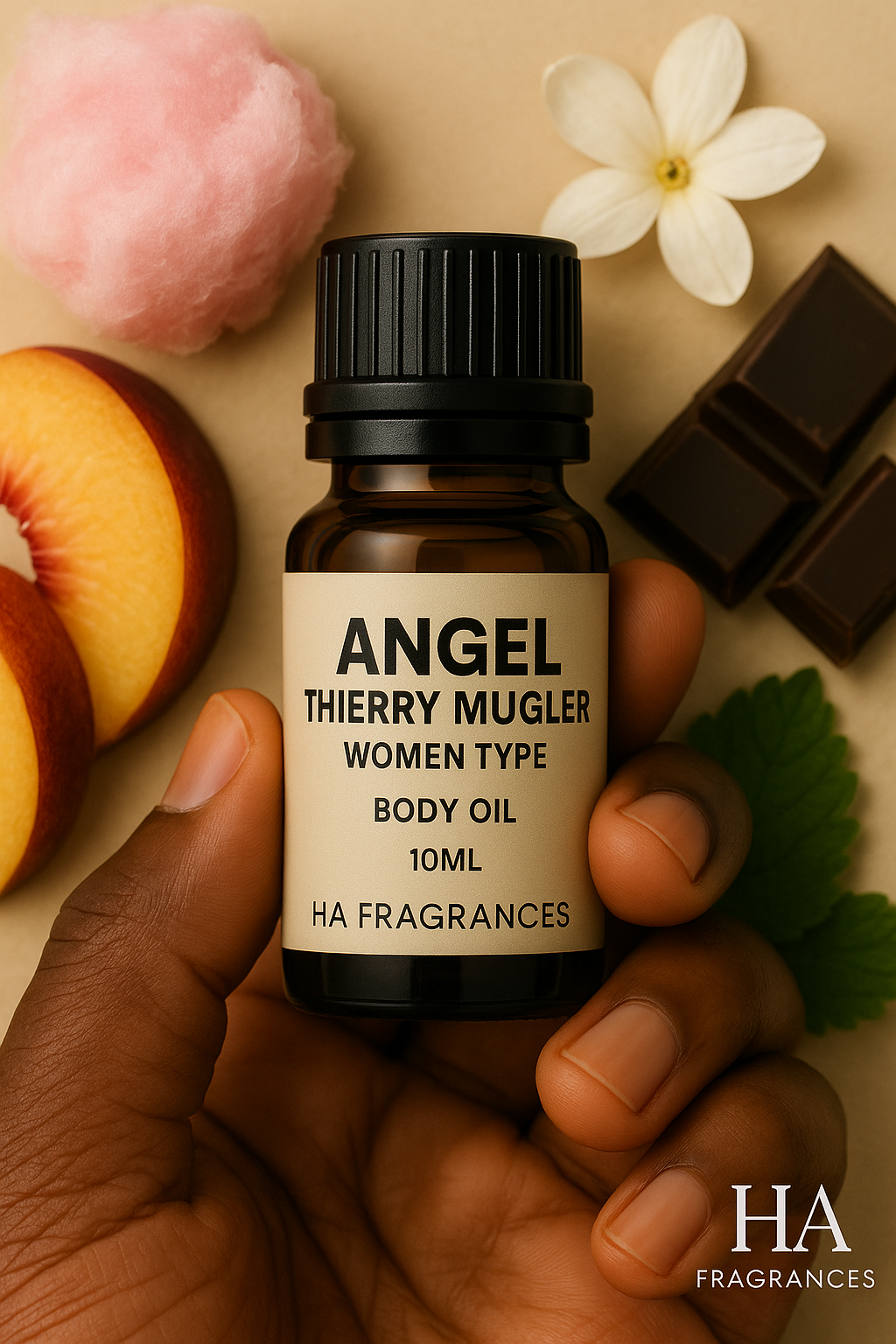 Dark-skinned hand holding a 10ml HA Fragrances Angel Thierry Mugler Women Type body oil bottle, surrounded by chocolate pieces, cotton candy, peach slices, jasmine flower, and green leaf on a beige background.