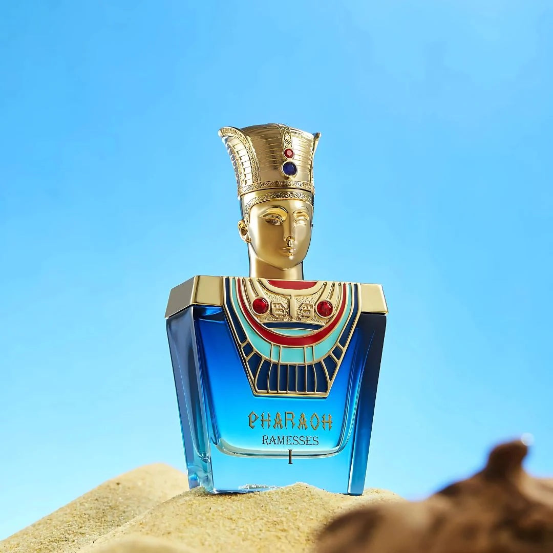 Pharaoh Ramesses I Eau De Parfum 100ML – a royal blue and gold perfume bottle with a pharaoh-inspired cap, set on sand with a bright sky backdrop.