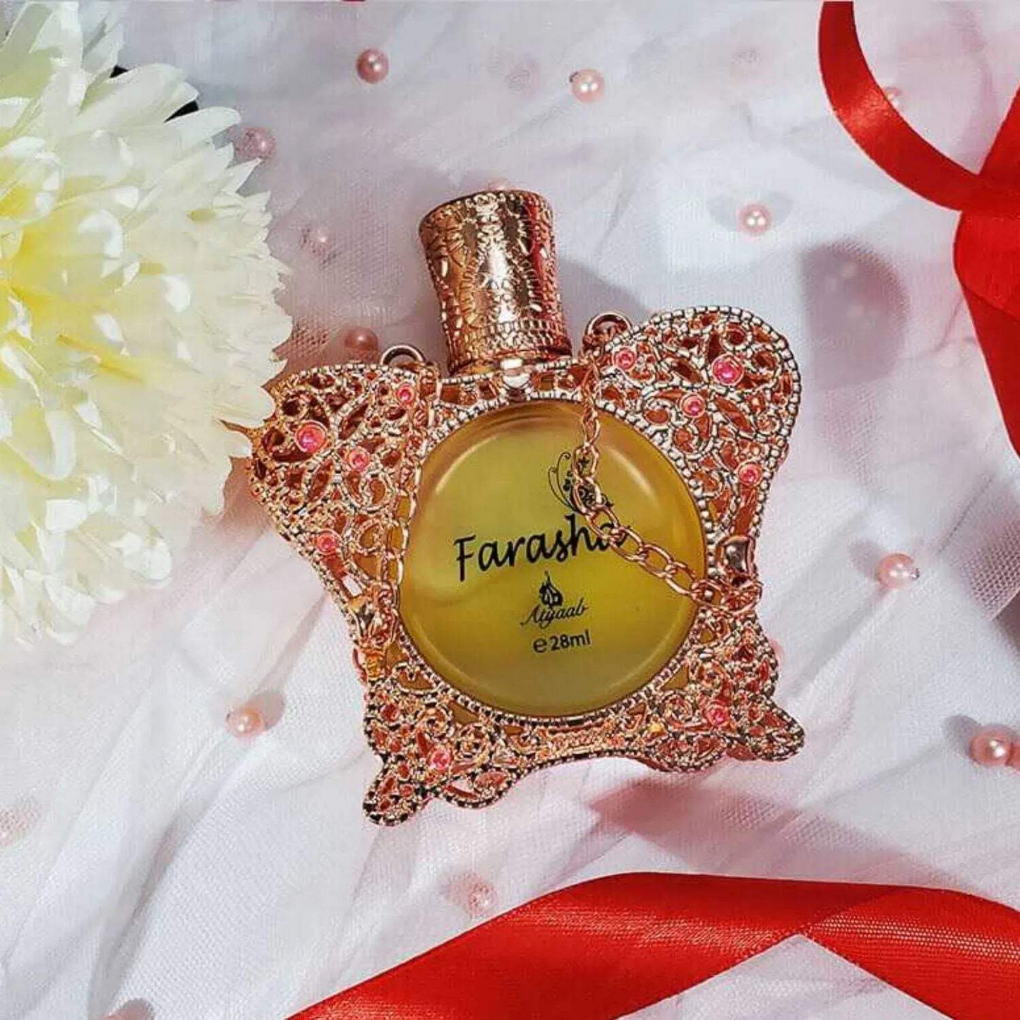 Farasha 28ml perfume oil by Khadlaj in a beautifully crafted rose gold bottle with intricate jewel and chain detailing, placed on a soft floral setting.