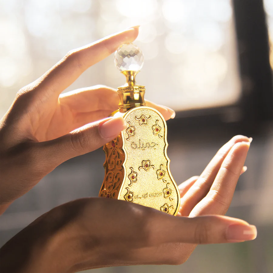 Jamila perfume bottle by Swiss Arabian, held elegantly in hands, showcasing its detailed golden design and crystal cap.