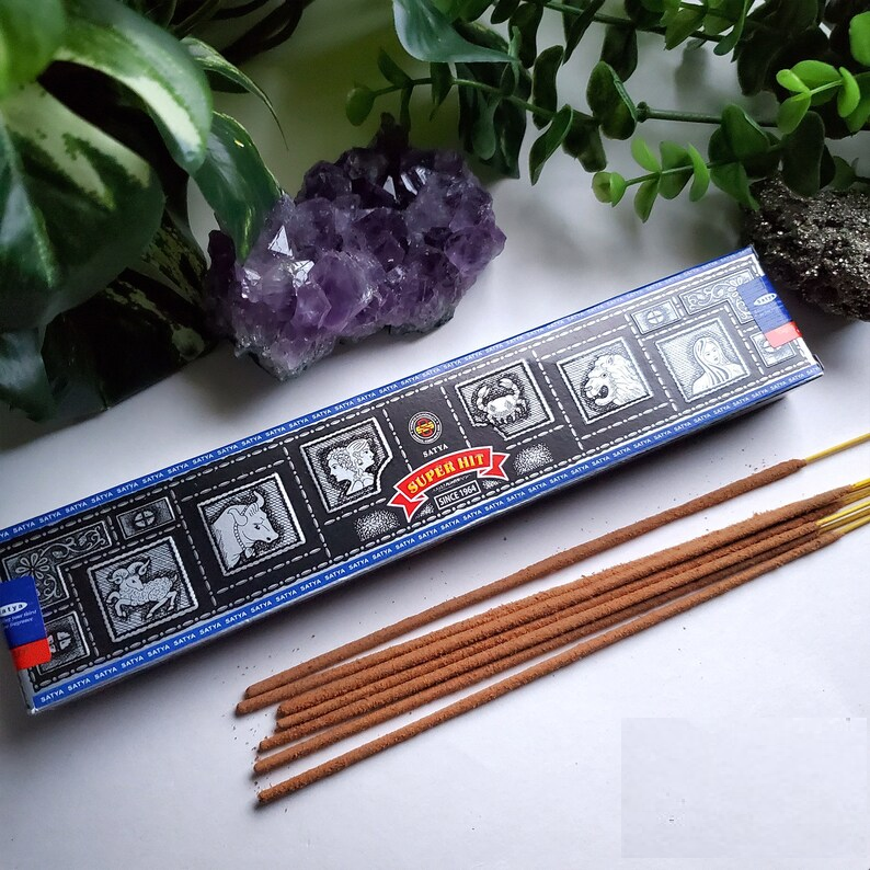 Satya Super Hit Incense 15g pack with hand-rolled incense sticks, displayed alongside natural greenery and a purple amethyst crystal, highlighting its luxurious and calming aroma.