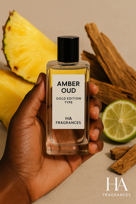 Dark-skinned hand holding HA Fragrances Amber Oud Gold Edition Type body oil bottle, surrounded by fresh pineapple slices, cinnamon wood sticks, and lime on a beige background – fresh, fruity, and woody fragrance image.