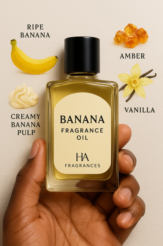 A clear bottle of Banana Fragrance Oil held by a dark-skinned hand, surrounded by ripe bananas and vanilla beans on a soft yellow background, with the HA Fragrances logo in the corner.