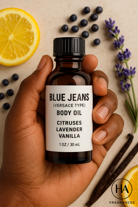 A bottle of Blue Jeans (Versace Type) Body Oil held by a dark-skinned hand, surrounded by citrus slices, juniper berries, lavender sprigs, and vanilla beans, with the HA Fragrances logo in the corner.