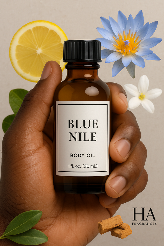 A bottle of Blue Nile Body Oil held by a dark-skinned hand, surrounded by citrus slices, water lily petals, jasmine flowers, and smooth sandalwood pieces, with the HA Fragrances logo in the corner.