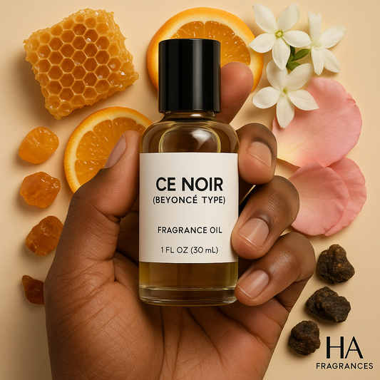A bottle of Ce Noir (Beyoncé Type) Body Oil held by a dark-skinned hand, surrounded by honey drizzles, clementine slices, jasmine petals, and amber stones, with the HA Fragrances logo in the corner.