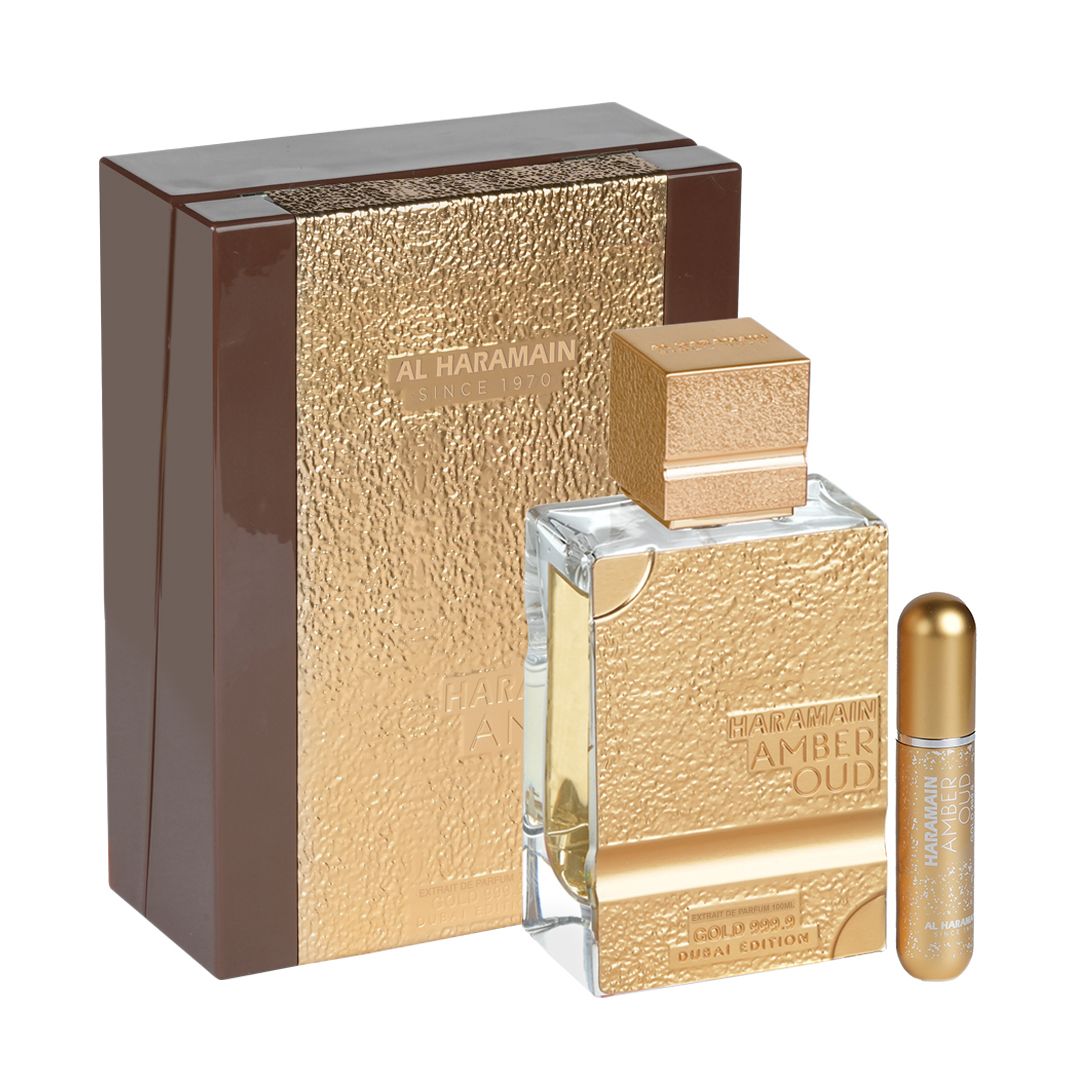 A luxurious bottle of Haramain Amber Oud Gold 999.9 Dubai Edition Extrait De Parfum, 100ml, displayed alongside its elegant gold-textured packaging and an additional atomizer.