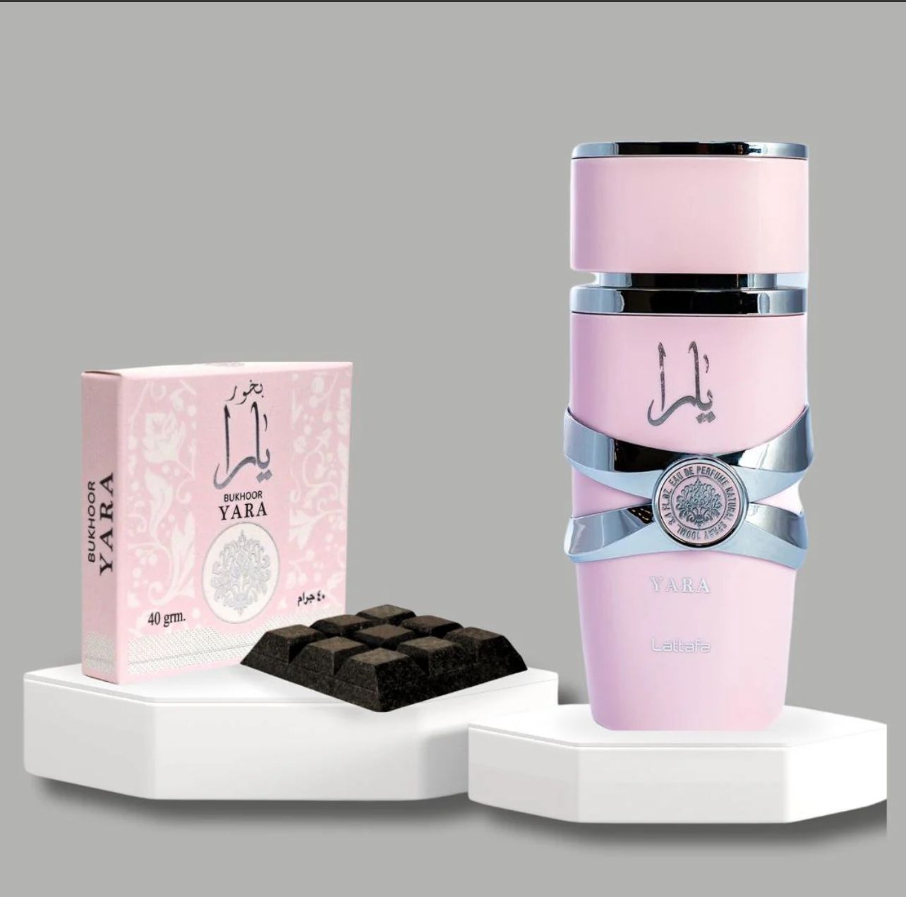 A Yara Perfume bottle in pastel pink with silver accents, displayed alongside a Yara Bukhoor box and Bukhoor pieces on a decorative stand.