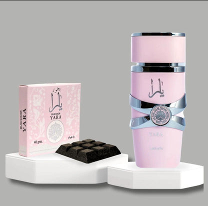 A Yara Perfume bottle in pastel pink with silver accents, displayed alongside a Yara Bukhoor box and Bukhoor pieces on a decorative stand.