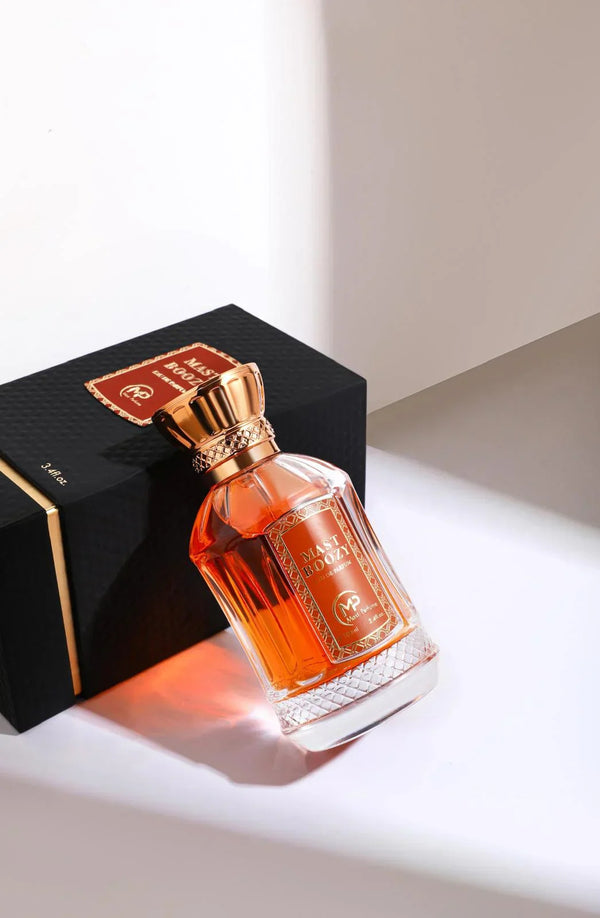 Mast Boozy Eau de Parfum bottle leaning on black gift box – amber glass design with gold cap, elegant gourmand scent featuring vanilla, caramel liqueur, and musk.