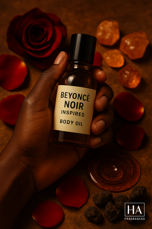 A bottle of Noir (Beyoncé Inspired) Body Oil held by a dark-skinned hand, surrounded by rose petals, amber resin, myrrh, and soft musk, with the HA Fragrances logo in the corner.