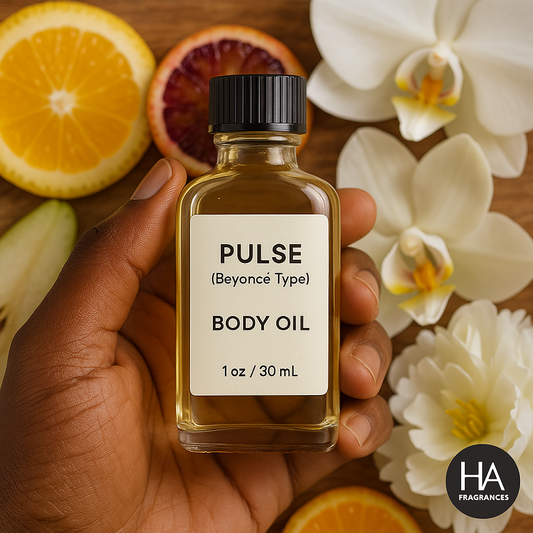 A bottle of Pulse (Beyoncé Type) Body Oil held by a dark-skinned hand, surrounded by orchid petals, sliced bergamot, pear blossoms, and vanilla beans, with the HA Fragrances logo in the corner.