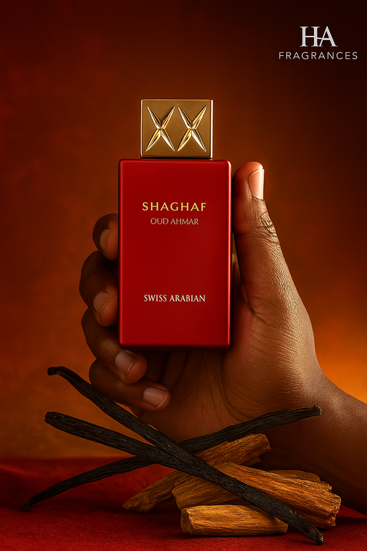 Dark-skinned hand holding Swiss Arabian Shaghaf Oud Ahmar Eau De Parfum bottle with warm amber glow, vanilla pods, and sandalwood pieces on a deep red-gold background with HA Fragrances logo.