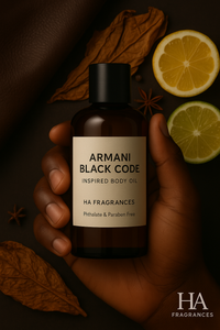 Dark-skinned hand holding HA Fragrances Armani Black Code Inspired Body Oil bottle with slices of lemon and lime, star anise, and dried tobacco leaves in the background – elegant masculine citrus and spicy fragrance visual.