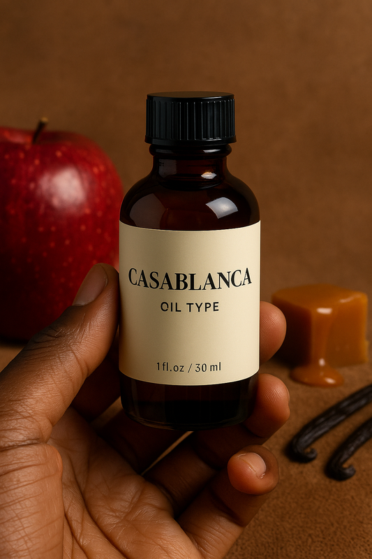 Casablanca Type fragrance oil bottle held by a dark-skinned hand, with a red apple, caramel cube, and vanilla pods in the background – Swiss Arabian inspired sweet and musky perfume oil.