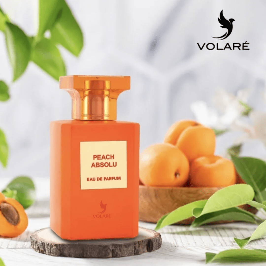 Peach Absolu Eau De Parfum 100ml by Volare, displayed in a sleek orange bottle surrounded by fresh peaches and greenery, symbolizing its fruity and luxurious fragrance.