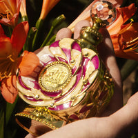 Stunning Yulali perfume bottle by Swiss Arabian held against vibrant orange flowers, showcasing its intricate design and luxury.